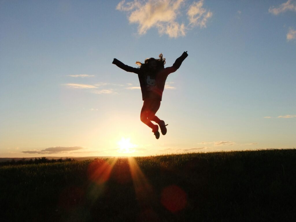 Changer de Banque simplement Silhouette of a young girl joyfully jumping against a vibrant sunset backdrop.